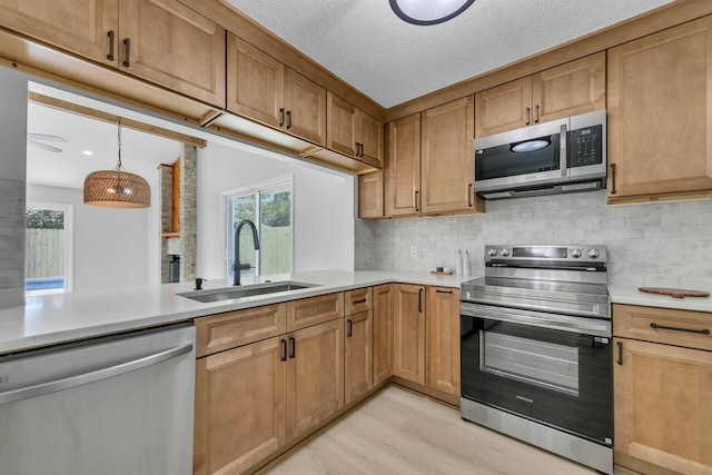 kitchen featuring light wood-style flooring, a sink, stainless steel appliances, light countertops, and decorative backsplash