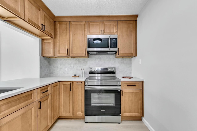 kitchen with light wood-style floors, tasteful backsplash, appliances with stainless steel finishes, and light countertops