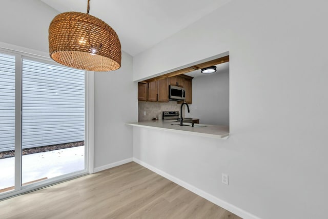 kitchen with light wood finished floors, decorative light fixtures, light countertops, vaulted ceiling, and appliances with stainless steel finishes