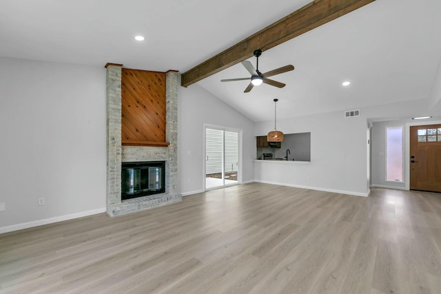 unfurnished living room with light wood finished floors, visible vents, a brick fireplace, and vaulted ceiling with beams