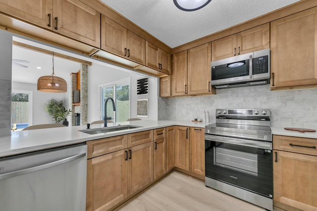 kitchen featuring light wood-type flooring, a sink, stainless steel appliances, light countertops, and decorative backsplash