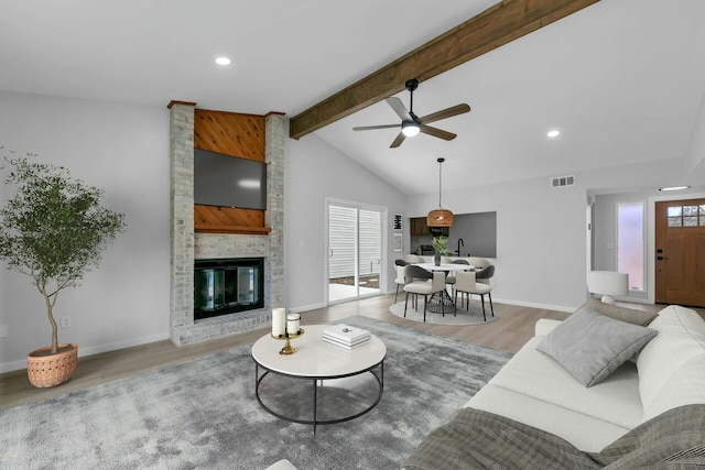 living area with visible vents, light wood finished floors, baseboards, lofted ceiling with beams, and a fireplace