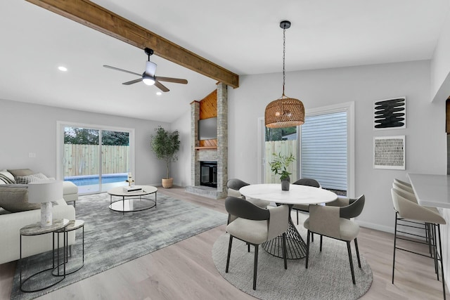 dining area featuring light wood-type flooring, a ceiling fan, a fireplace, baseboards, and vaulted ceiling with beams