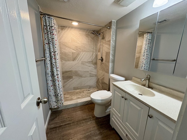 full bath featuring toilet, wood finished floors, vanity, visible vents, and a tile shower