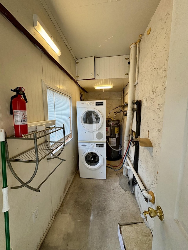 laundry area with laundry area, water heater, and stacked washing maching and dryer