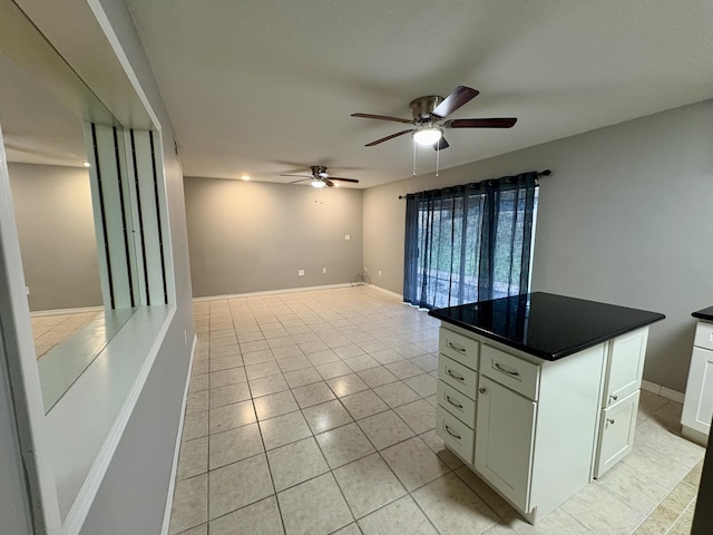 interior space with light tile patterned floors, ceiling fan, baseboards, white cabinets, and dark countertops