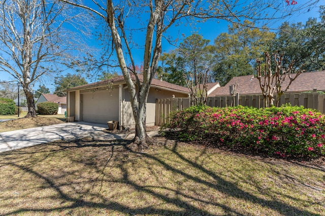 view of property exterior with an attached garage, concrete driveway, a yard, and fence