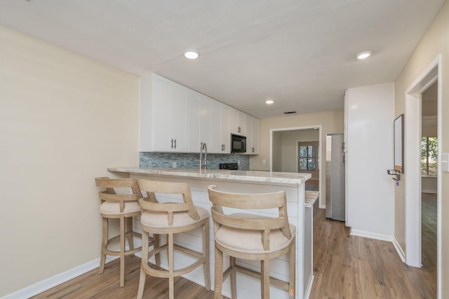 kitchen with backsplash, black microwave, a peninsula, freestanding refrigerator, and white cabinets