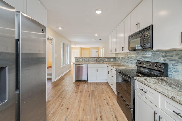 kitchen with a peninsula, light wood-style flooring, black appliances, white cabinetry, and tasteful backsplash