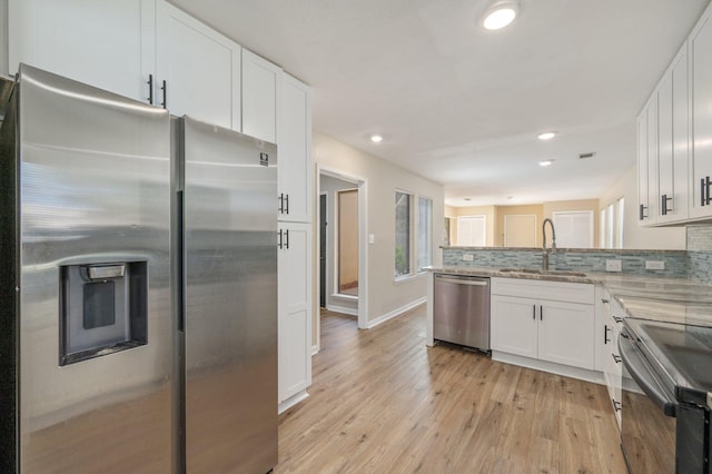 kitchen featuring a sink, decorative backsplash, stainless steel appliances, white cabinetry, and light wood-type flooring