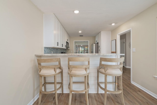 kitchen with tasteful backsplash, baseboards, a kitchen bar, wood finished floors, and white cabinets