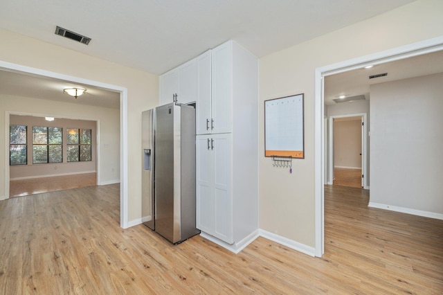 kitchen with visible vents, stainless steel fridge, white cabinets, and light wood-style flooring