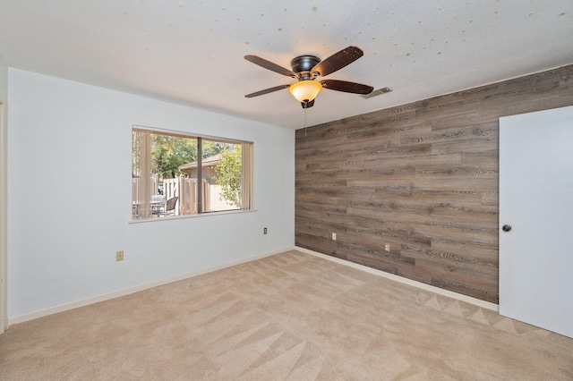 spare room with wooden walls, visible vents, baseboards, carpet, and a ceiling fan