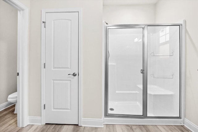 bathroom featuring toilet, wood finished floors, a stall shower, and baseboards