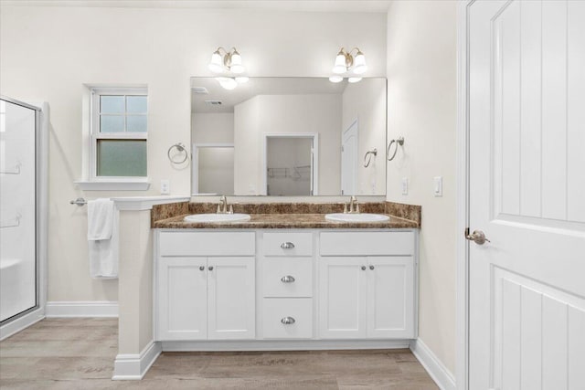 full bath featuring a shower stall, wood finished floors, double vanity, and a sink