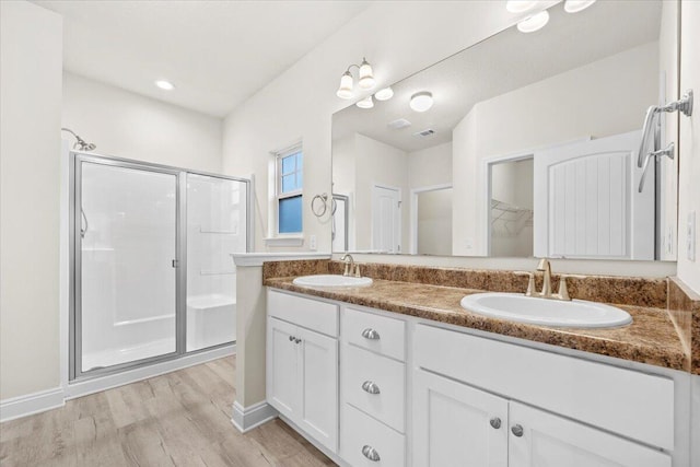 bathroom with double vanity, wood finished floors, a stall shower, and a sink