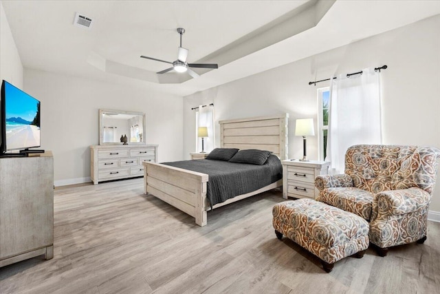 bedroom featuring light wood finished floors, visible vents, a raised ceiling, and baseboards