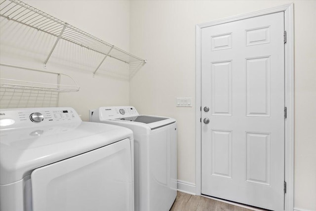 clothes washing area with laundry area, light wood-style flooring, separate washer and dryer, and baseboards