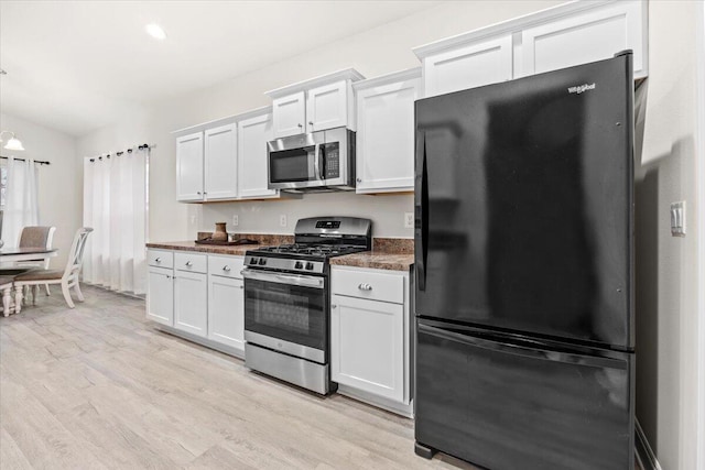 kitchen featuring dark countertops, light wood-type flooring, hanging light fixtures, white cabinets, and stainless steel appliances