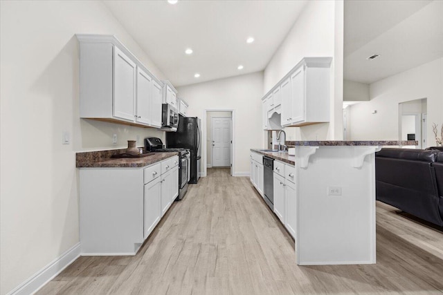 kitchen with light wood-type flooring, a sink, a kitchen breakfast bar, dark countertops, and stainless steel appliances