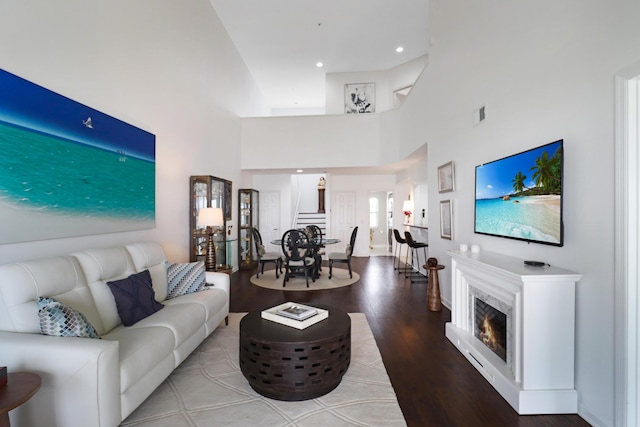 living room with visible vents, a warm lit fireplace, wood finished floors, recessed lighting, and a towering ceiling