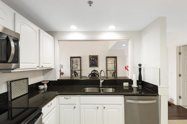 kitchen featuring a sink, white cabinetry, stainless steel appliances, dark stone counters, and a peninsula