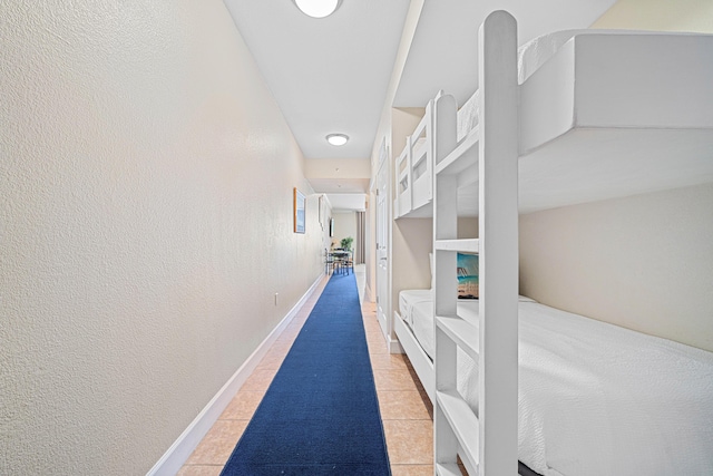 hallway featuring light tile patterned floors, baseboards, and a textured wall