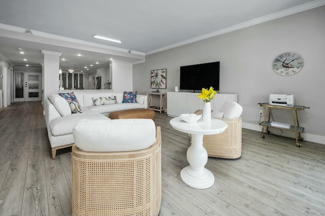 living area with crown molding, wood finished floors, baseboards, and ornate columns