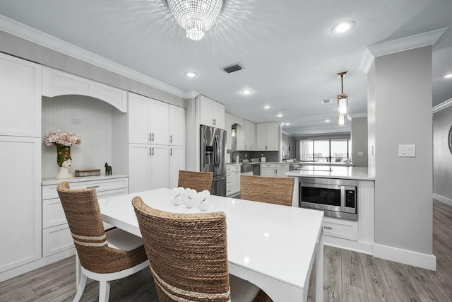 kitchen featuring visible vents, ornamental molding, a kitchen island, appliances with stainless steel finishes, and white cabinets