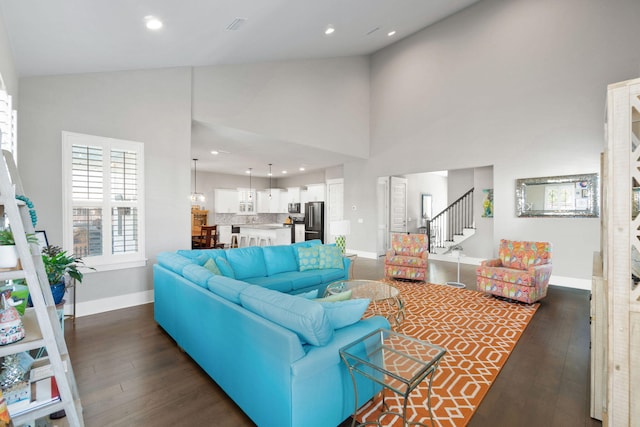 living area with high vaulted ceiling, dark wood-style flooring, stairway, and baseboards