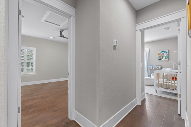 hall featuring attic access, visible vents, dark wood finished floors, and baseboards