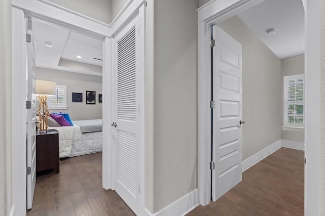 hall with a raised ceiling, recessed lighting, dark wood finished floors, and baseboards