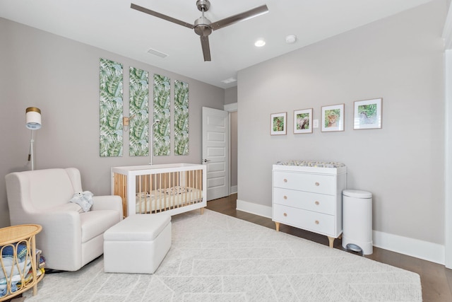 bedroom featuring a crib, wood finished floors, visible vents, and baseboards