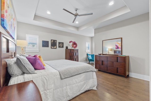 bedroom with a raised ceiling, multiple windows, baseboards, and wood finished floors