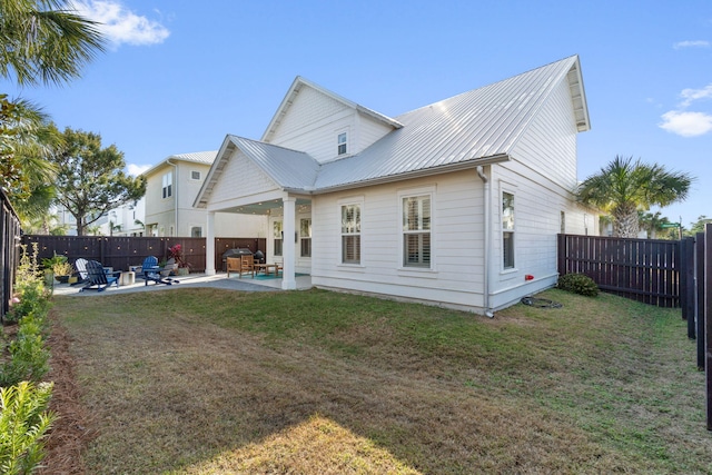 rear view of house with a patio area, metal roof, a fenced backyard, and a lawn