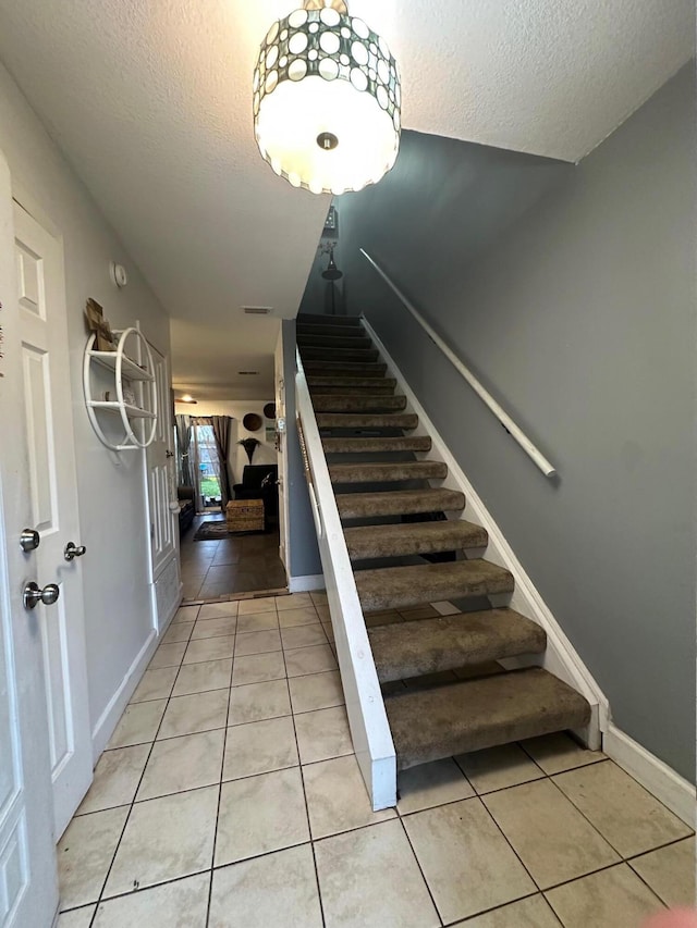 staircase featuring a textured ceiling, baseboards, and tile patterned floors