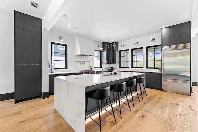 kitchen with modern cabinets, visible vents, premium range hood, and stainless steel built in refrigerator