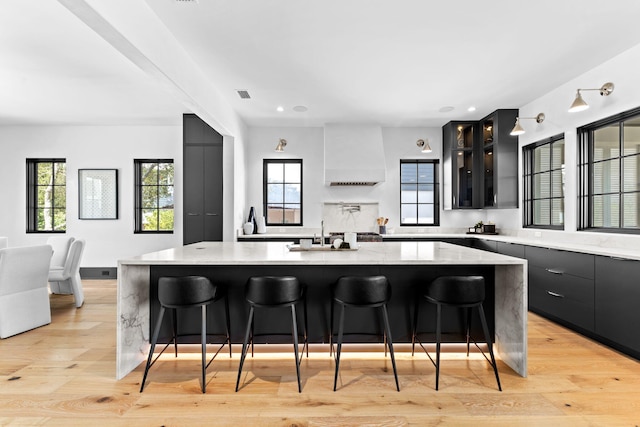 kitchen featuring custom exhaust hood, visible vents, light wood-style flooring, and a sink