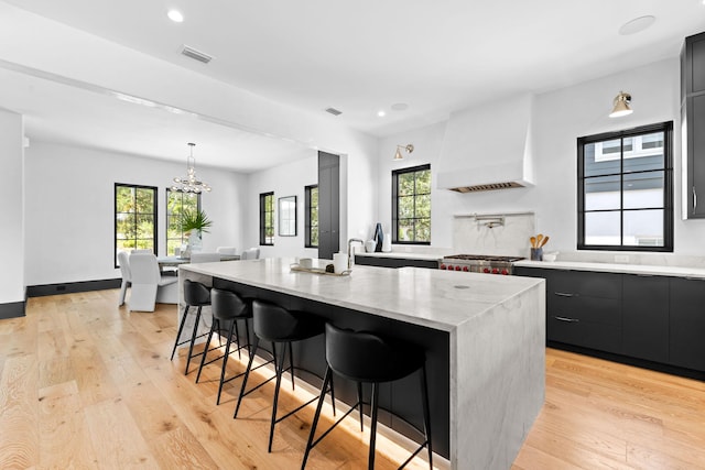 kitchen featuring visible vents, a kitchen breakfast bar, light wood-type flooring, and premium range hood