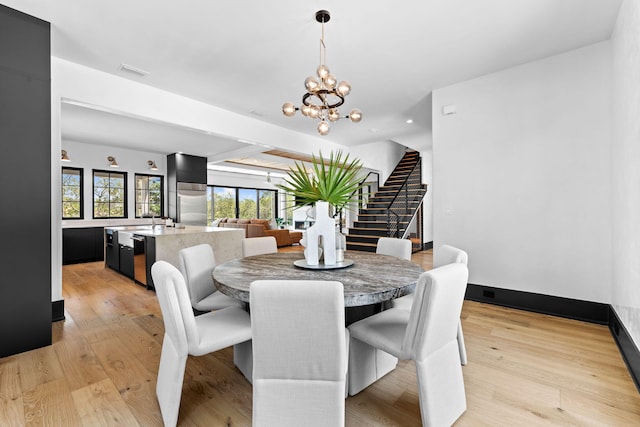 dining room featuring light wood finished floors, stairway, baseboards, and an inviting chandelier