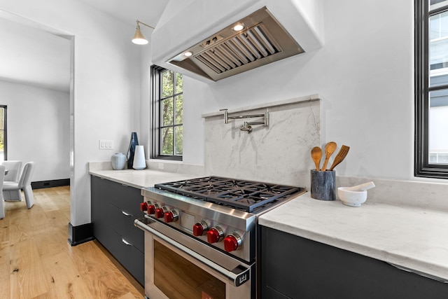 kitchen with high end stainless steel range oven, custom exhaust hood, dark cabinets, and light wood finished floors