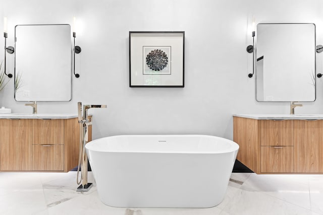 full bath featuring a soaking tub, two vanities, marble finish floor, and a sink