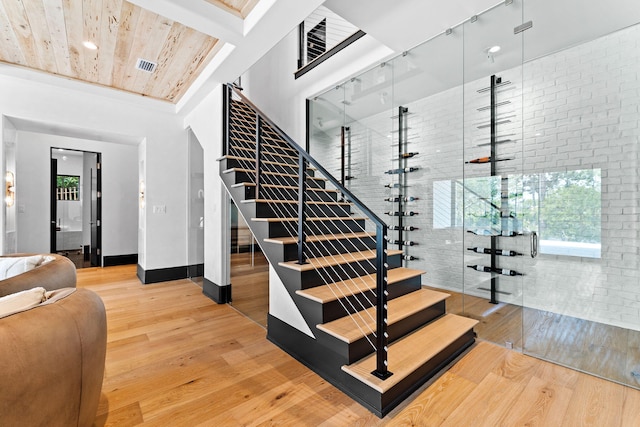 stairs with visible vents, brick wall, and wood finished floors