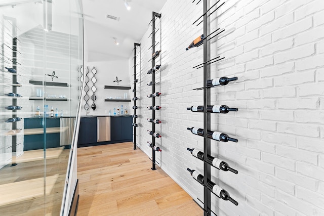 wine room featuring light wood finished floors, visible vents, and brick wall