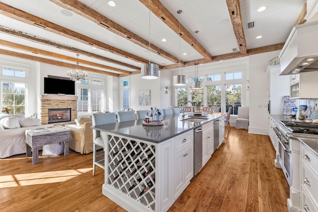 kitchen with a stone fireplace, high end stove, a sink, white cabinetry, and an island with sink