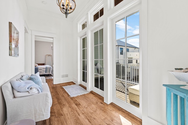 doorway to outside featuring crown molding, baseboards, wood finished floors, and a notable chandelier