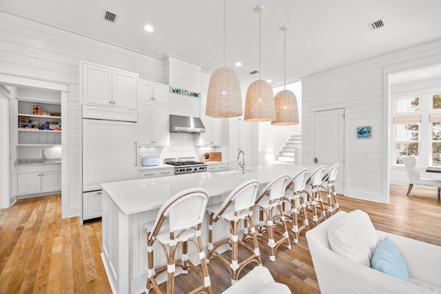 kitchen featuring gas stove, light countertops, a kitchen breakfast bar, wall chimney exhaust hood, and light wood-type flooring