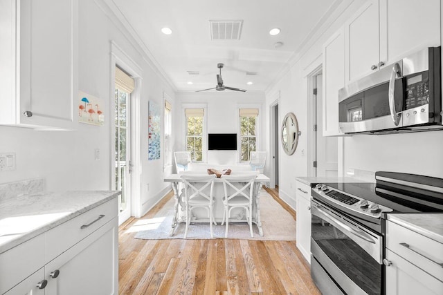 kitchen with visible vents, ornamental molding, stainless steel appliances, light wood-style floors, and white cabinetry