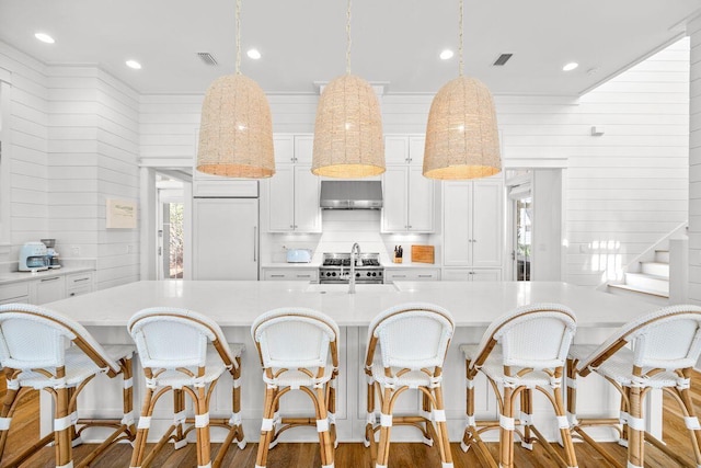 kitchen featuring wood finished floors, visible vents, light countertops, wall chimney range hood, and premium appliances