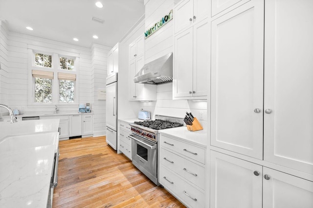 kitchen featuring high end appliances, recessed lighting, light wood-style floors, white cabinetry, and wall chimney range hood